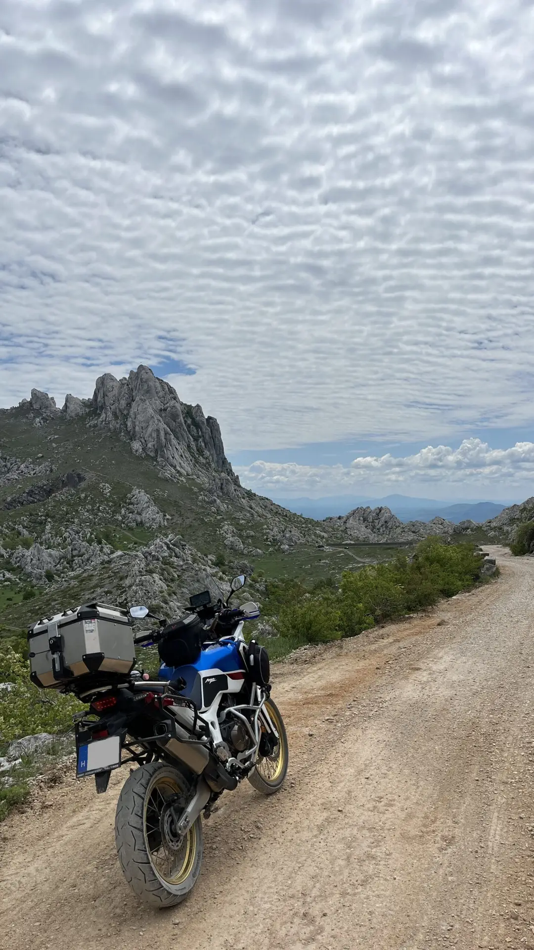 Motoros megáll egy szerpentines úton – túramotor, napsütéses panoráma és hegység.